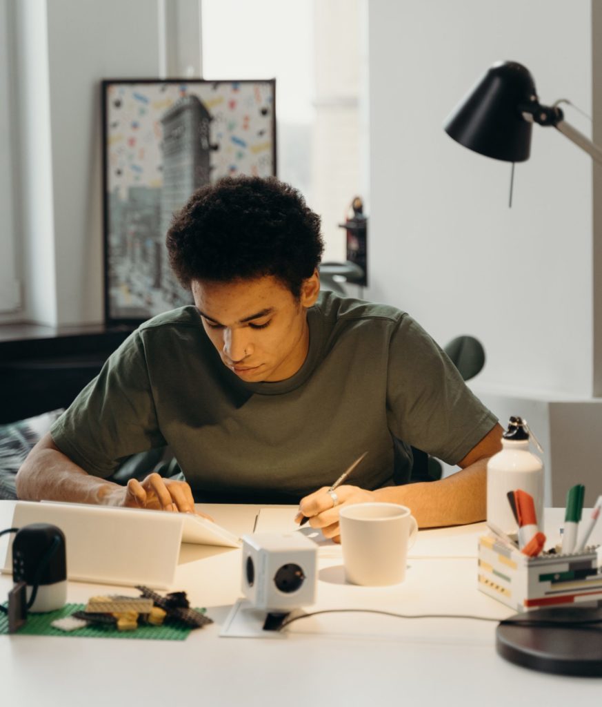 a young man draws at a desk with a tablet, surrounded by creative tools