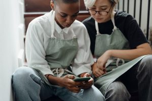 two people wearing aprons looking at mobile phone