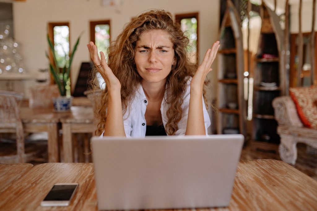 woman looking frustrated with hands up in front of a laptop