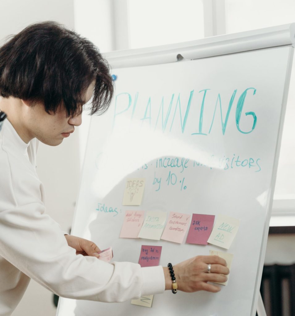 young asian man arranges planning notes on a white board
