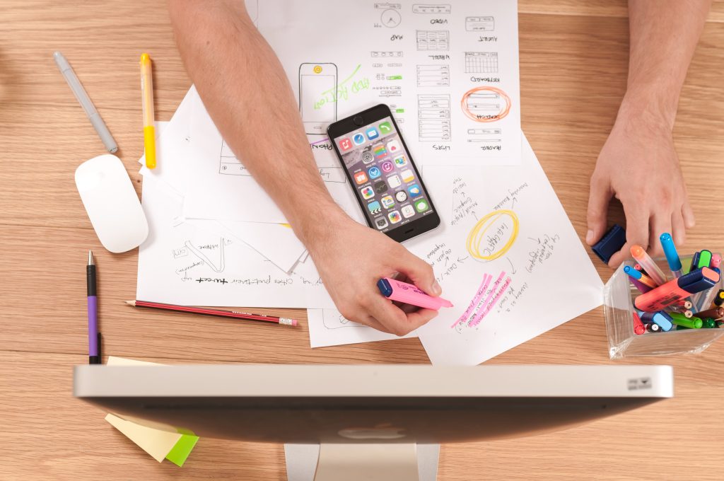 hands holding a highlighter above papers and a mobile phone