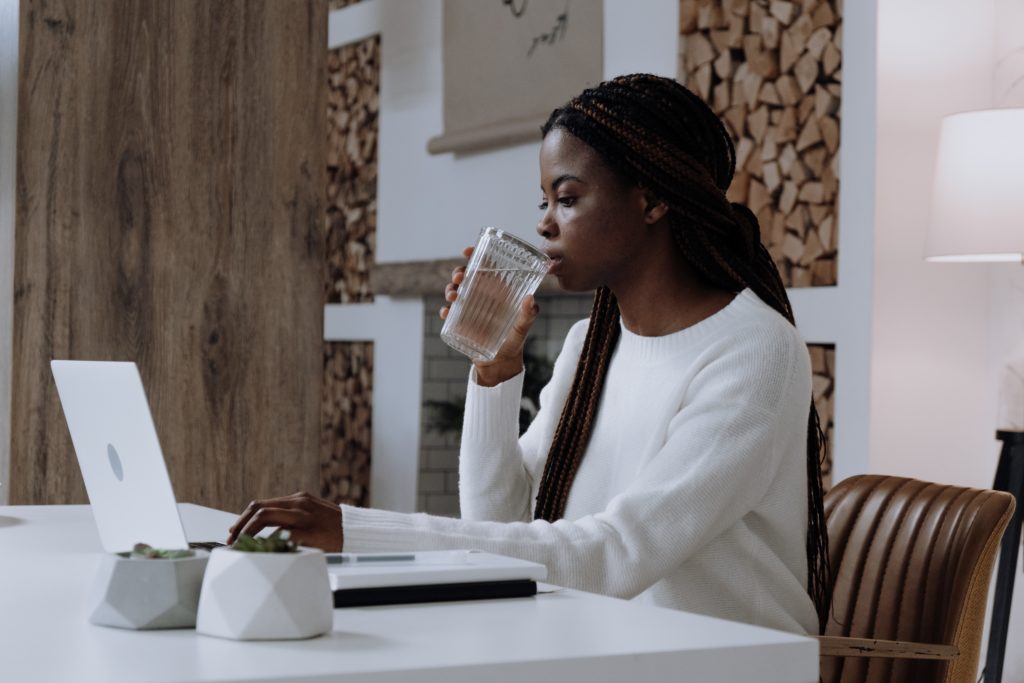 black woman sitting at a table drinking water and looking at a laptop