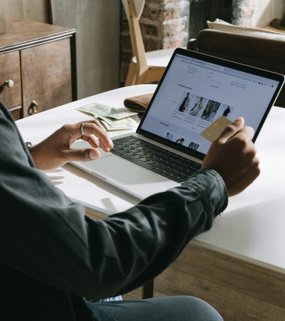 partial view of a person sitting at a desk with a laptop and a credit card in one hand