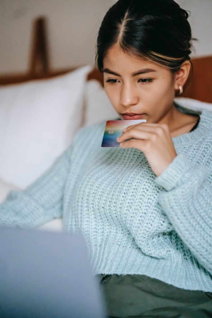 woman holding a credit card looking pensive at a laptop screen